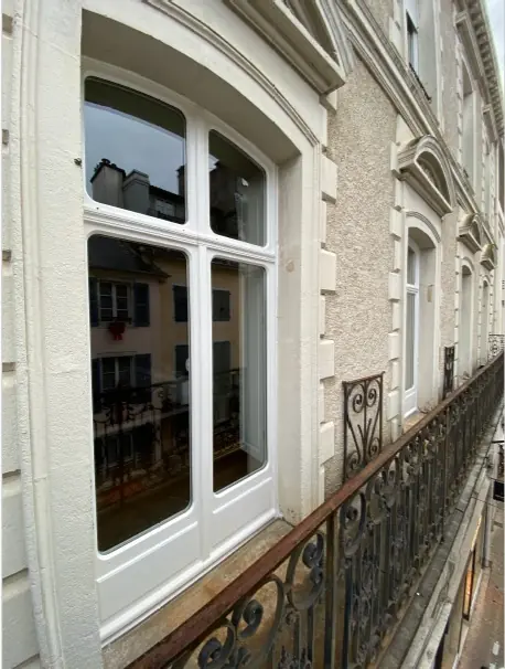 Fenêtre bois blanche à imposte cintrée sur une façade en pierre avec balcon en fer forgé (Menuiserie Feugas)