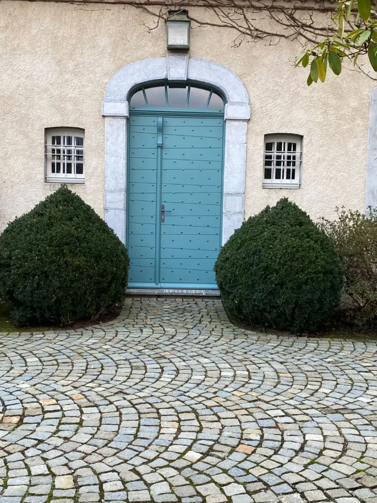 Porte d’entrée bois cloutée bleue sous une imposte cintrée vitrée, dans un encadrement de pierre (Menuiserie Feugas)