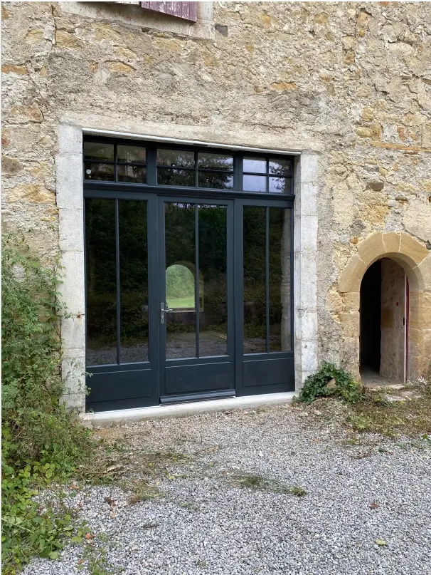 Ensemble vitré bois gris anthracite avec porte-fenêtre, fixes latéraux et imposte, dans un mur de pierre (Menuiserie Feugas)