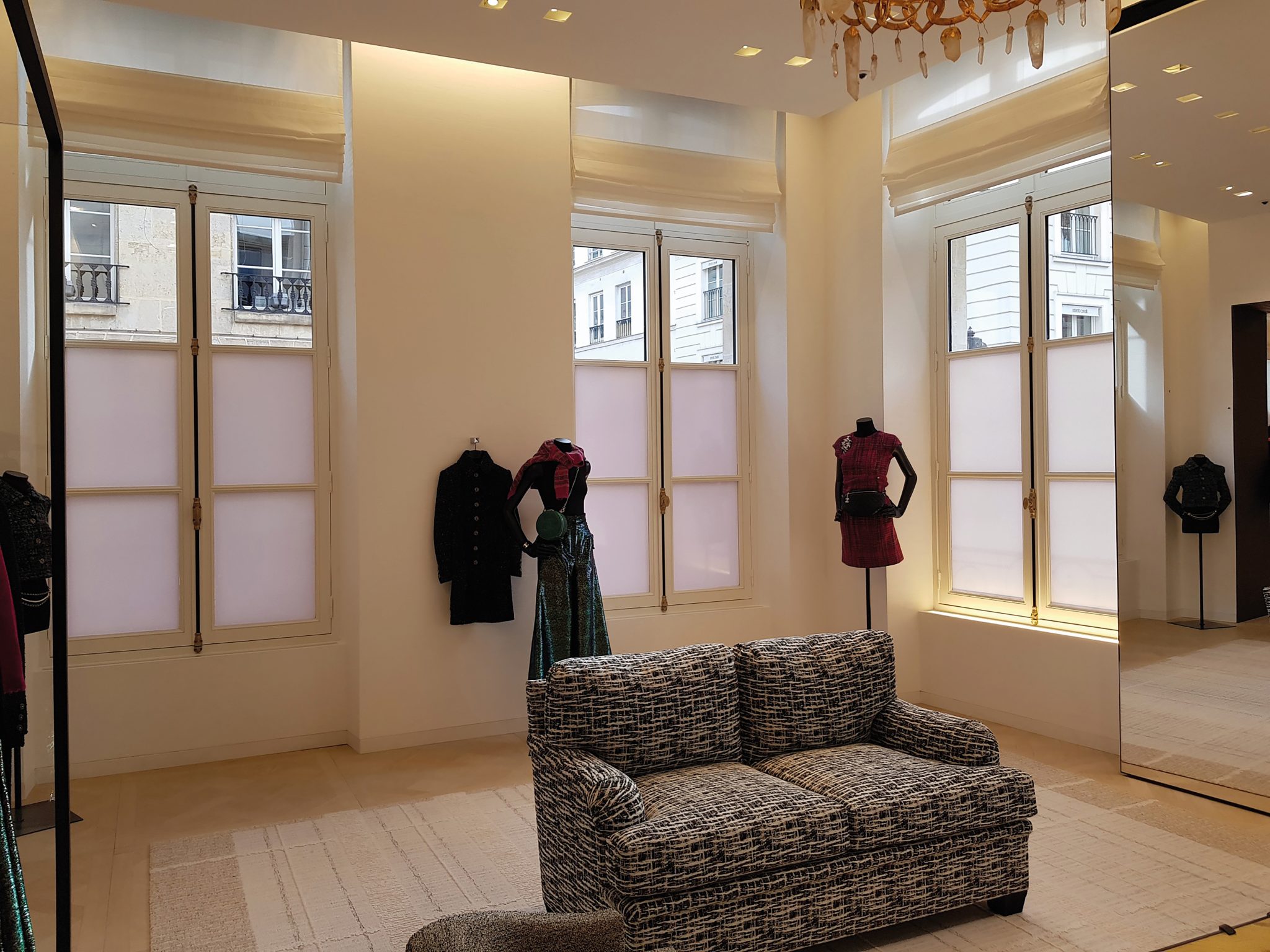 Pièce claire éclairée par trois hautes fenêtres en bois équipées de stores, donnant sur des immeubles parisiens