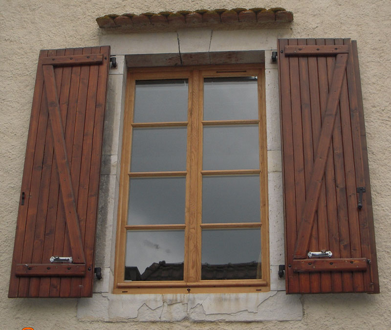 Fenêtre en bois à deux vantaux encadrée de volets battants en bois lasuré, sur une façade enduite