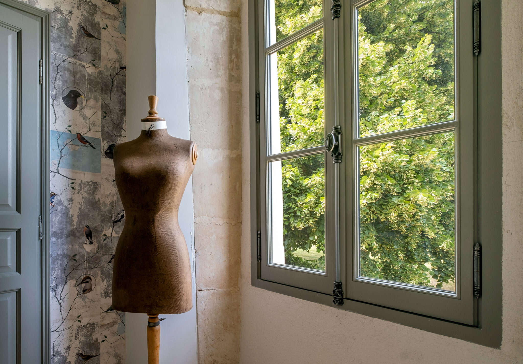 Fenêtre en bois à deux vantaux peinte en vert de gris, vue de l’intérieur à côté d’un mannequin de couture